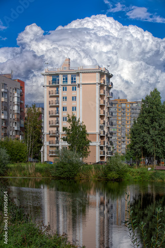 Public city park with pond and reeds and multi-storey dwelling buildings behind under blue sky with amazing clouds at sunny autumn day © Igor Groshev