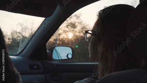 A girl with glasses rides in the car in the front seat and looks into the distance. Back view. © Vital9c