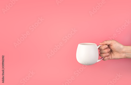 A woman's hand holds a white mug on a pink background. Background with space to copy, side view.