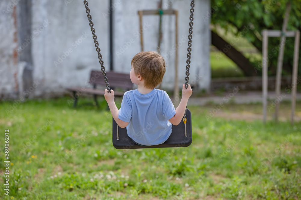 Little boy ride on a swing in the child playground. Little baby boy hand holding tightly on a metallic chain while going on a swing at a playground. Rear view Little boy ride on a swing in the child playground. Little baby boy hand holding tightly on a metallic chain while going on a swing at a playground. Rear view