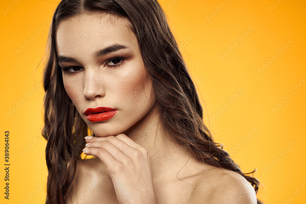 Beautiful brunette naked shoulders bright makeup red lips hairstyle close-up yellow background Beautiful brunette naked shoulders bright makeup red lips hairstyle close-up yellow background