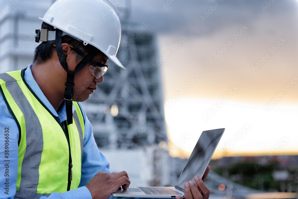 Civil Engineer wearing high visibility safety vest and helmet while using laptop looking to drawing detail on the terrace of decaying building at construction site. Surveyor for renovation concept. Civil Engineer wearing high visibility safety vest and helmet while using laptop looking to drawing detail on the terrace of decaying building at construction site. Surveyor for renovation concept.