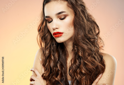 Attractive woman model on a pink background hugs herself with her hands and bright makeup brunette curls