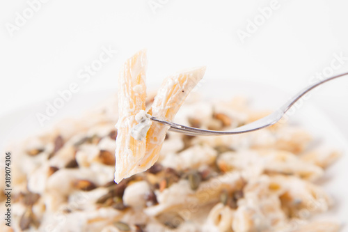 Pasta with blue cheese and cream sauce, sprinkled with roasted pumpkin seeds eaten with a fork