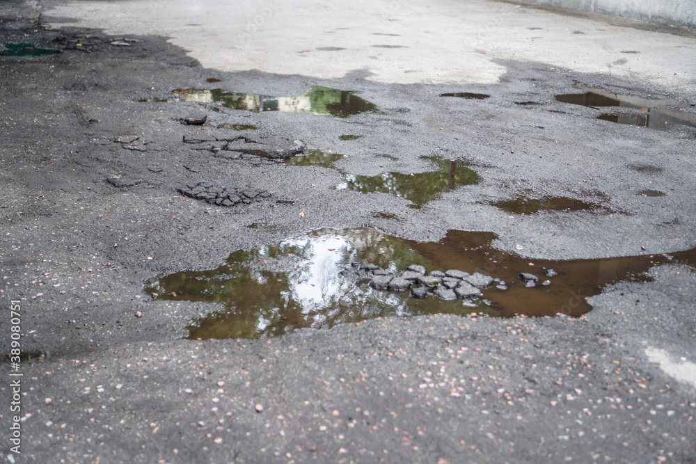 Destroyed road in poor condition requiring repair. Holes in the asphalt are filled with water and puddles. Stock photo background
