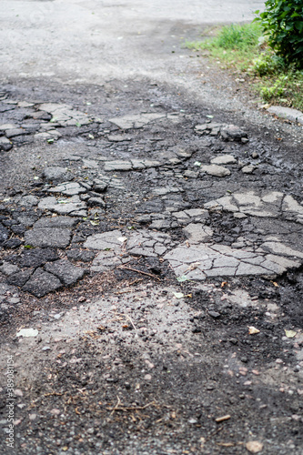 Destroyed road in poor condition requiring repair. Holes in the asphalt are filled with water and puddles. Stock photo background