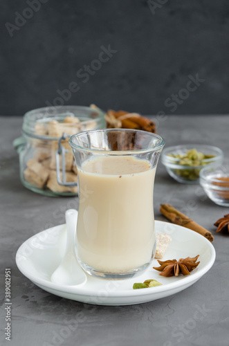 Hot tea with milk  cinnamon  cardamom  anise and other spices  Indian masala tea in a glass on a dark background. Vertical  copy space.