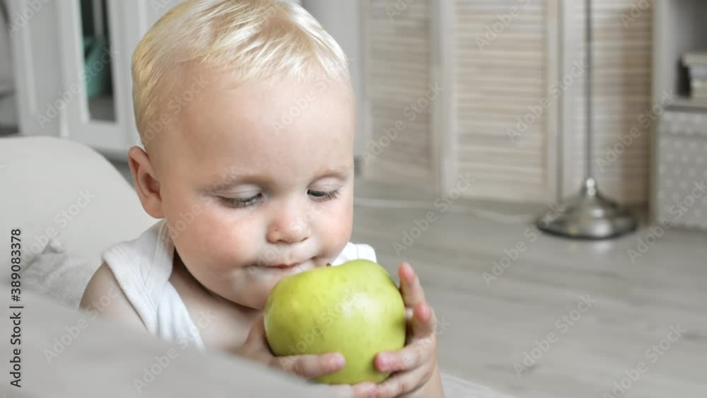 Close up of adorable Caucasian baby boy with blond hair and blue eyes sitting on couch at home, plying and laughing Close up of adorable Caucasian baby boy with blond hair and blue eyes sitting on couch at home, plying and laughing