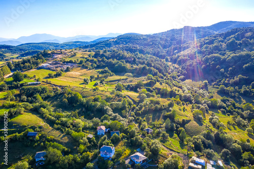 Aerial view from drone of beautiful mountain hills with houses and trees. Photo with sun flares © EdVal