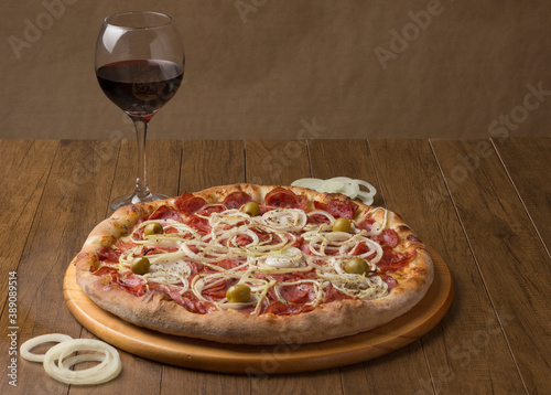 Pepperoni sausage pizza with sliced ​​onions, and green olives. Glass of Red Wine. Brazillian tipical food. Similar to Pepperonie's pizza. Photography with space for texts.