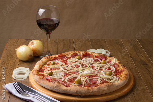 Pepperoni sausage pizza with sliced ​​onions and green olives. Glass of red wine and rustic onions. Brazillian tipical food. Similar to Pepperonie's pizza. Close-up photography.