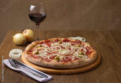Pepperoni sausage pizza with slices of onions and green olives. Glass of red wine and rustic onions. Brazillian tipical food. Similar to Pepperonie's pizza. Photography with space for texts.