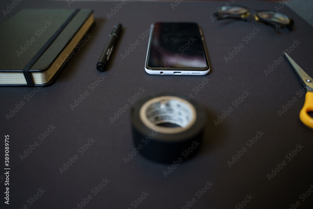 Work area on a black table, smartphone, scissors, pen, book, notebook, glasses Work area on a black table, smartphone, scissors, pen, book, notebook, glasses
