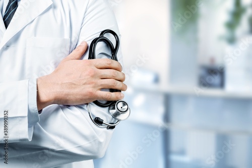 Young man doctor holding stethoscope on background