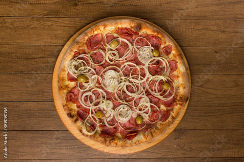 Photo of a pepperoni pizza, slices of onions, mozzarella cheese and green olives. On a wooden board. Horizontal photography. Pizza in the center.