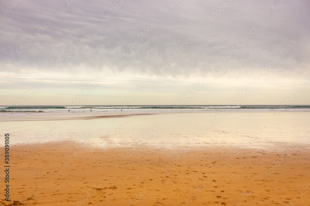 Wide panoramic beach with dramatic sky, bay of Biscay. Surf concept. Idyllic surfing day in Spain. Seascape with waves and surfers. Active lifestyle. Cloudy seascape. 