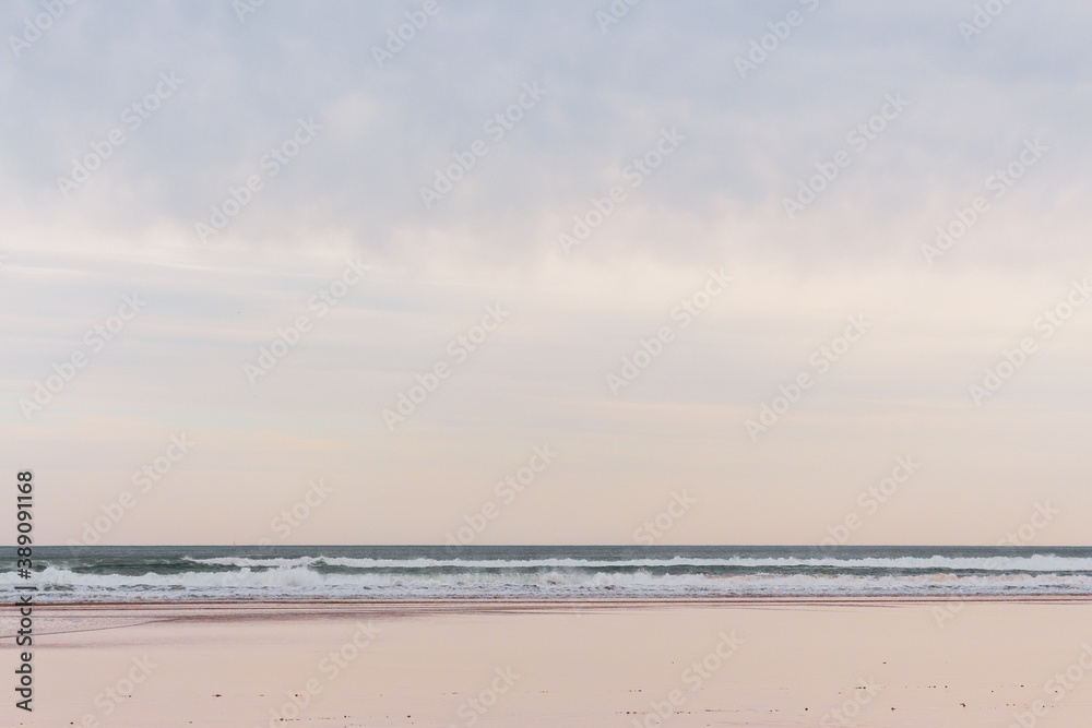 Wide empty beach with wet sand and copy space, bay of Biscay. Surf concept. Scenic seascape with waves and empty beach. Coastline with reflection at wet sand. Dramatic sky over autumn beach. 