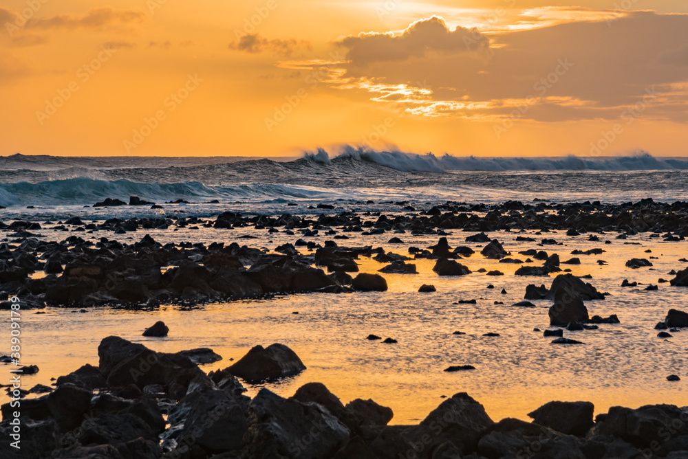 Orange sunset over ocean with waves and lava rock beach shoreline Orange sunset over ocean with waves and lava rock beach shoreline