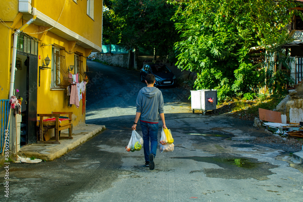 A man is coming back from shopping and walking on the street while carrying plastic bags.
