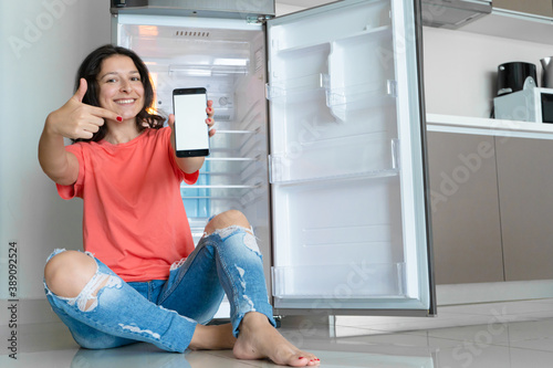 A girl orders food using a smartphone. Empty refrigerator with no food. Food delivery service advertisement