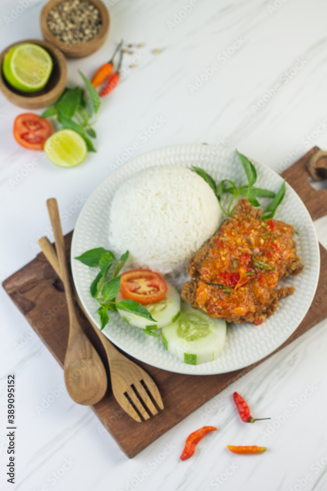 Ayam geprek, Indonesian popular streed food, made from crispy chicken smashed with sambal or chili sauce, eat with rice and cucumber, lettuce, tomato and kemangi. Isolated background, copy space.