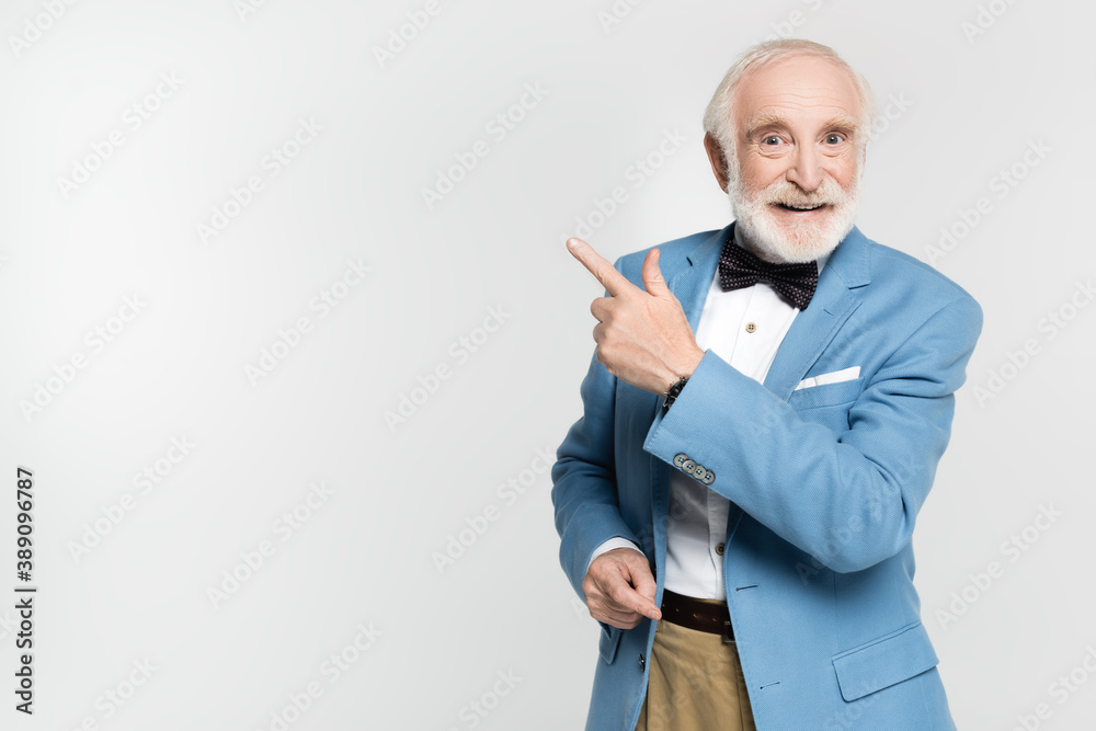 Smiling senior man in bow tie and jacket pointing with finger isolated on grey Smiling senior man in bow tie and jacket pointing with finger isolated on grey