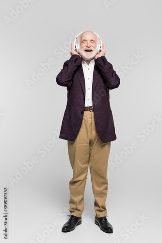 Cheerful senior man listening music in headphones on grey background