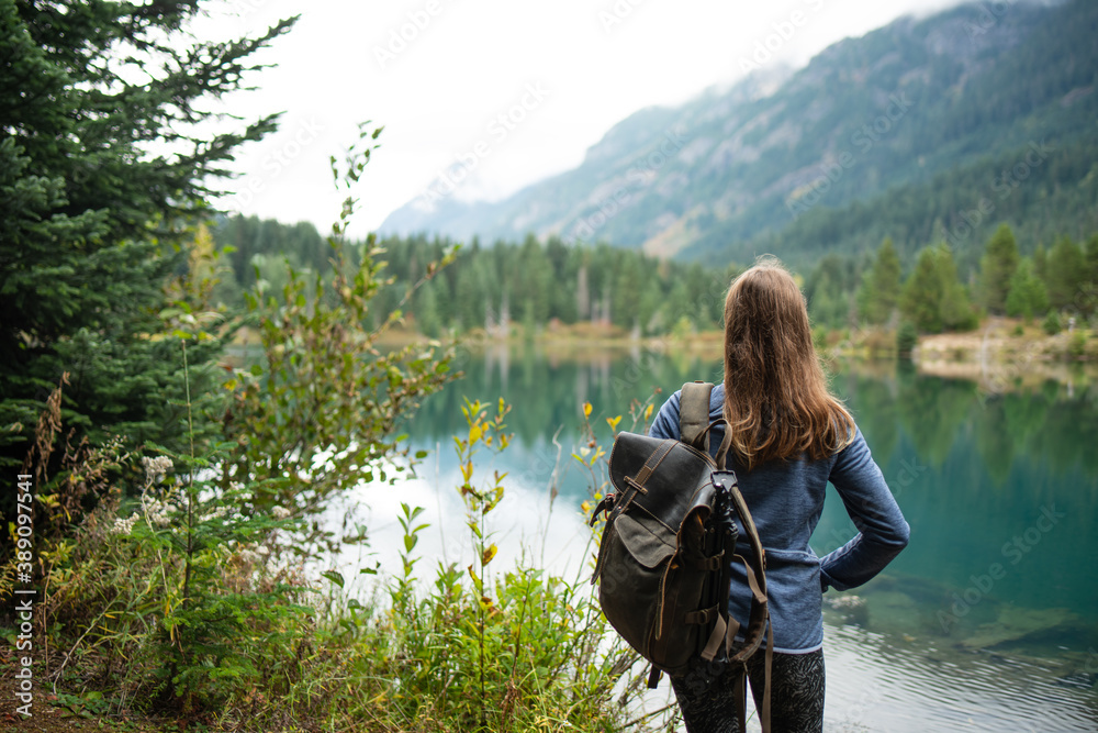 Back view of young woman with backpack near azure lake on wooded mountains background. Amazing landscape. Enjoying nature. Back view of young woman with backpack near azure lake on wooded mountains background. Amazing landscape. Enjoying nature.