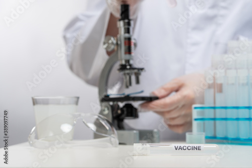 Microbiologist examines a covid-19 vaccine using microscope on laboratory background. Backstage of scientific discovery. Healthcare and medical concept.