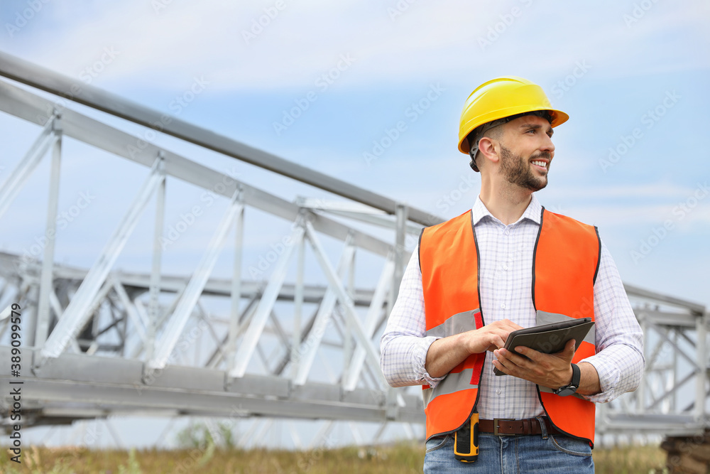 Professional engineer with tablet near high voltage tower construction outdoors. Installation of electrical substation