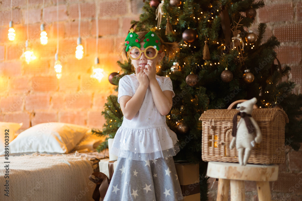 .Funny little girl in mask-glasses with a fir-tree on a christmas background