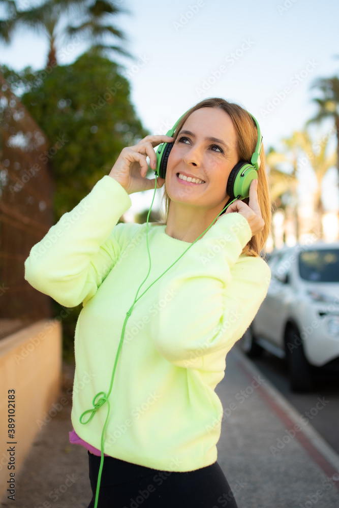 Young woman in sport wear enjoys and smiles listening music with green earphones