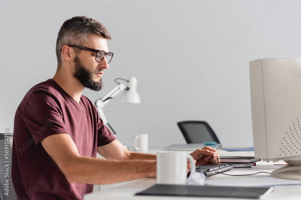 Businessman in casual wear using computer near stationery on blurred foreground in office Businessman in casual wear using computer near stationery on blurred foreground in office