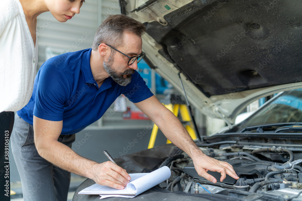 The mechanic doing engine checking with the customer observation nearby at the car auto service The mechanic doing engine checking with the customer observation nearby at the car auto service