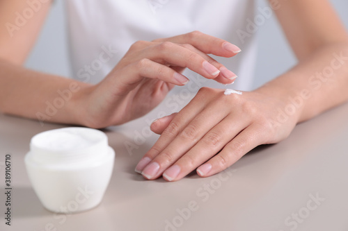 Young woman applying hand cream at table  closeup