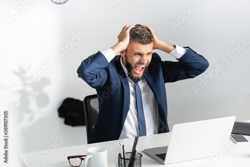 Businessman screaming and touching head during nervous breakdown in office