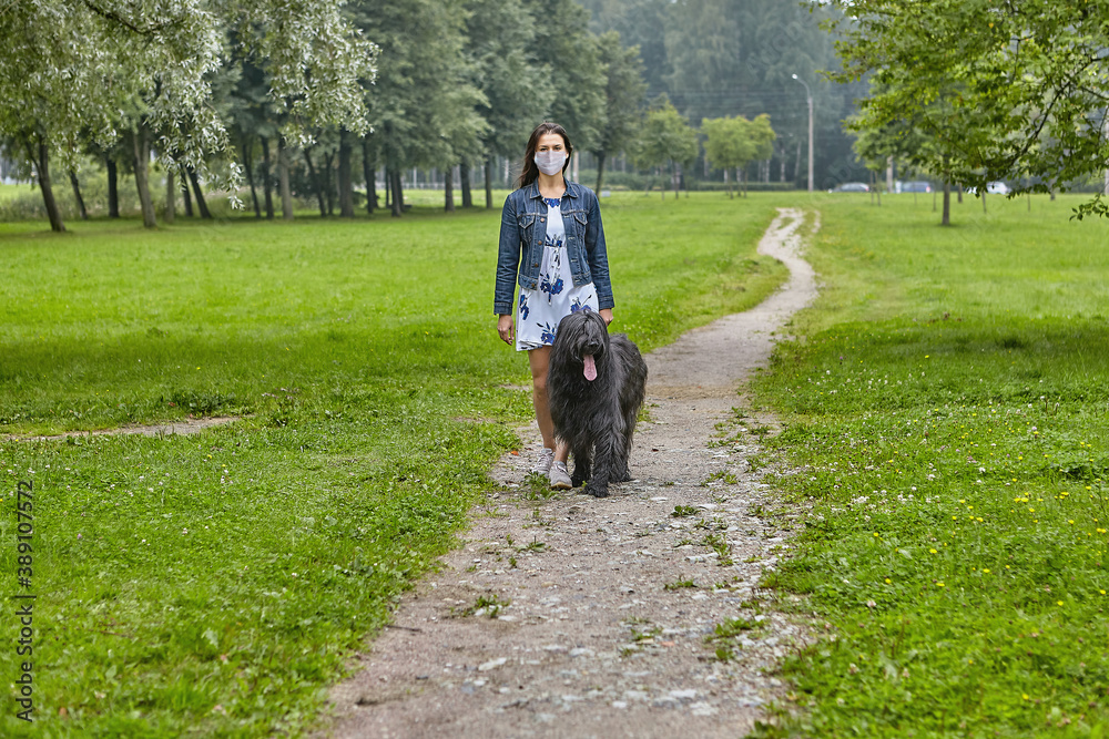White woman walks with black briard in facial mask on open air.