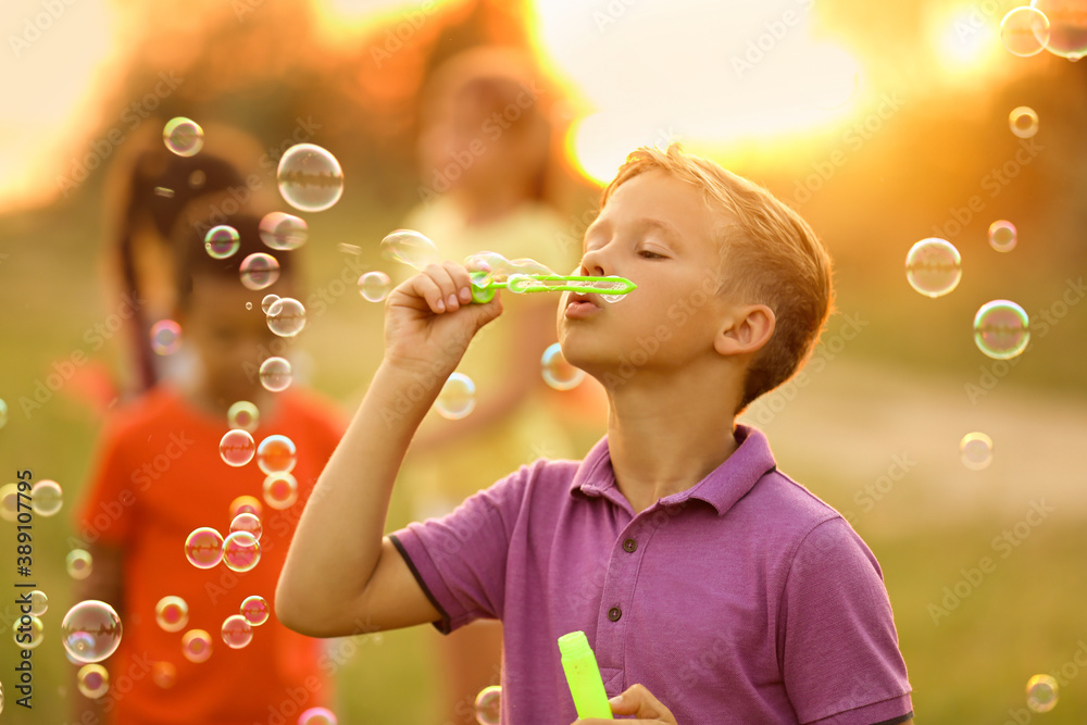 Cute little boy blowing soap bubbles outdoors at sunset Cute little boy blowing soap bubbles outdoors at sunset
