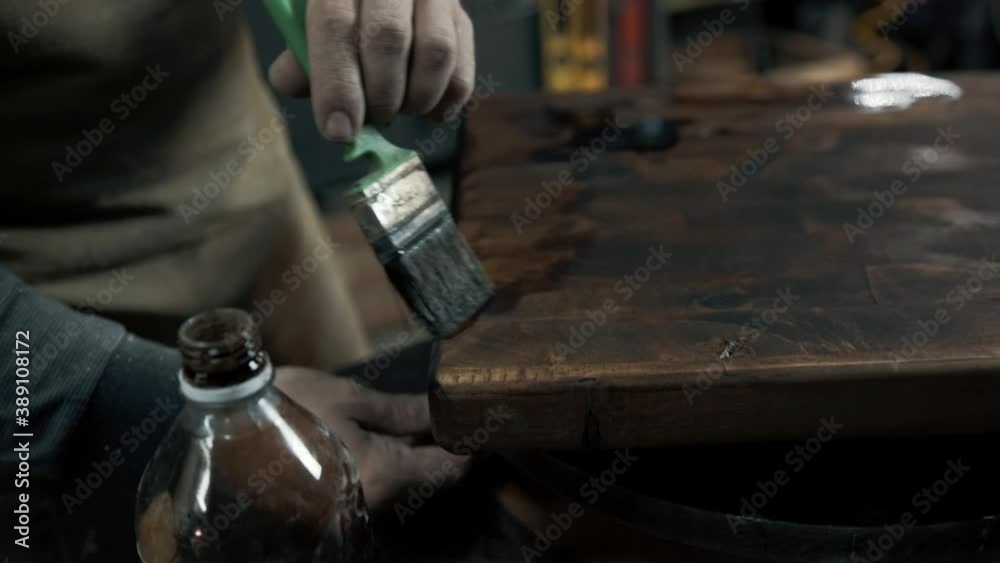 A carpenter paints a piece of wood for a loft-style chair with a brush. Close up A carpenter paints a piece of wood for a loft-style chair with a brush. Close up
