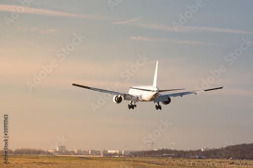 Airplane landing at airport in sunny day, back view. Silhouette of passenger aircraft almost landed at the runway. Vacation, aviation