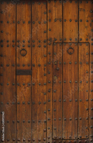 ancient and worn medieval door gate with rivets and knockers on a rough wooden texture surface - entrance of a chapel