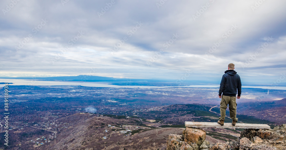 Adventurous man standing on top of a bench looking at the open landscape on a cloudy day.