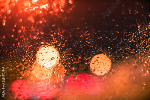 Abstract bokeh blur background by rain drops on glass window at night in the city
