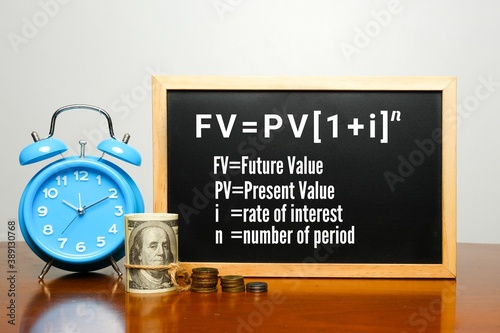 A picture of alarm clock, fake cash, coins and blackboard with time value of money formula on table. 1 dollar in future is not equivalent to today value. 