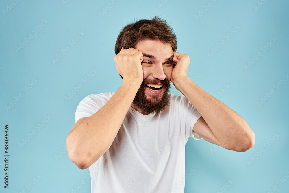 Emotional man with a beard in a white t-shirt blue background fun lifestyle Emotional man with a beard in a white t-shirt blue background fun lifestyle