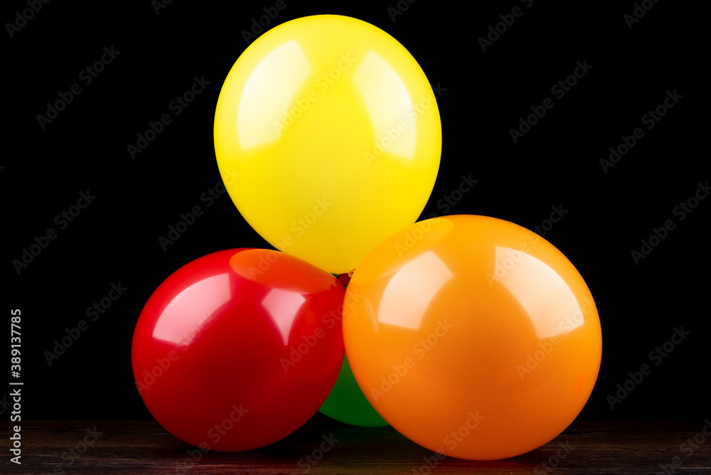 Bunch of colorful balloons on a wooden table against a black background.