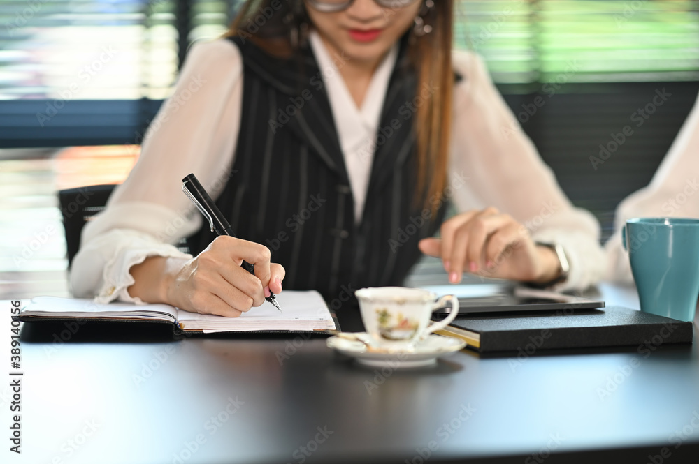 A female office worker working with computer tablet and writing on notebook in modern office.