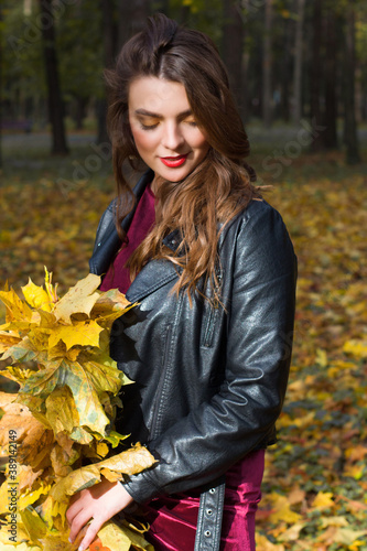 Young brunette woman portrait in autumn color. Yellow leaves in hand.