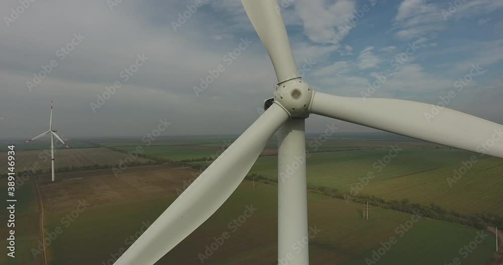 Aerial view a Windmill. Wind generator with slowly rotating blades against background of agricultural fields Aerial view a Windmill. Wind generator with slowly rotating blades against background of agricultural fields