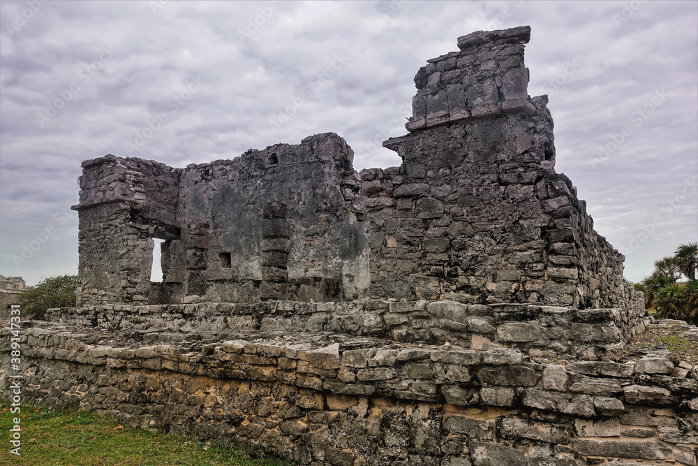 Ruins of the ancient Mayan city of Tulum. A dilapidated stone building rises against a cloudy sky. Memory of a bygone civilization. Mexico.